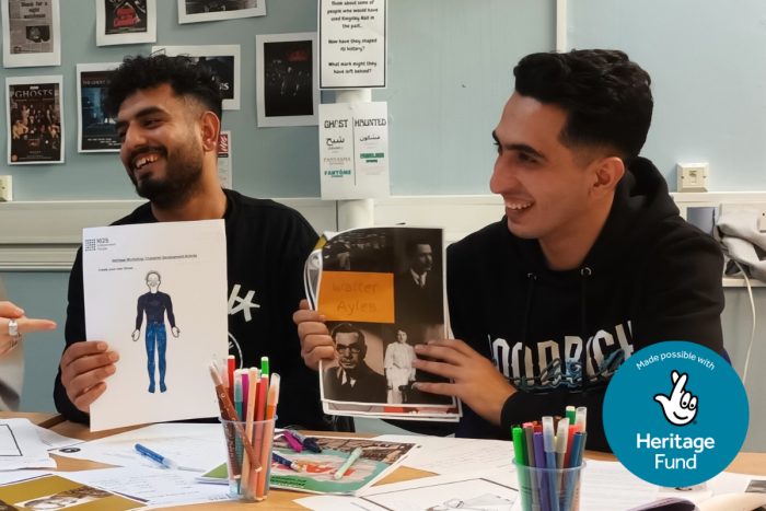Two members of the Heritage Youth Board smiling and holding up collages they have created in a Heritage workshop.