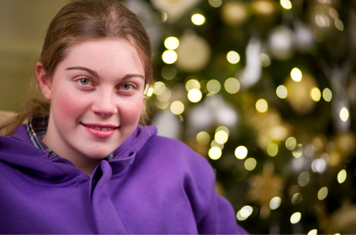 A young person smiling in front of a Christmas tree.