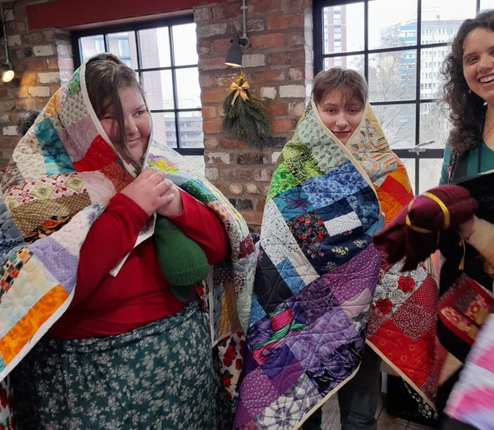 A group of young people wearing colourful quilts over their heads and shoulders.
