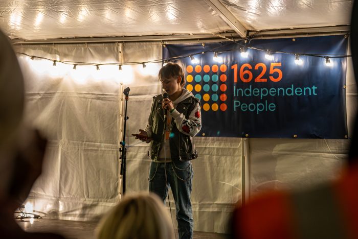 A young person standing on a stage in a tent speaking into a microphone.