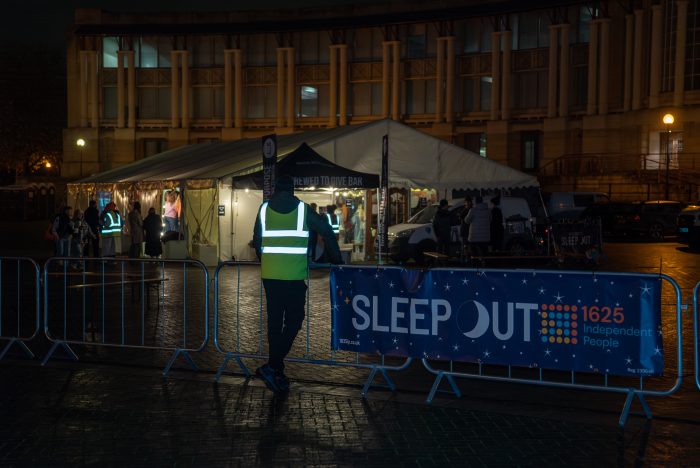 A person in a high-vis standing outside a big white tent at night.