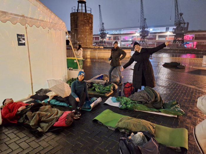 A group of people standing outside a tent next to sleeping bags